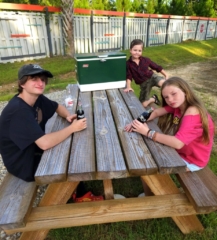 Three young kids at a picnic table with retro glass Coca-Cola bottles