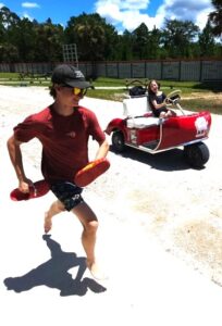 Young boy running along side retro golf cart driven by young girl